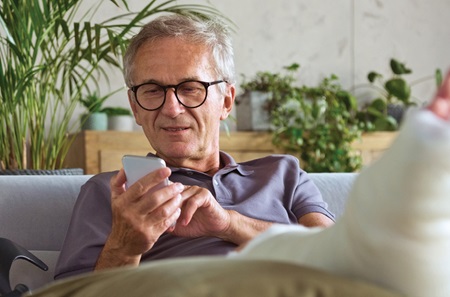 Man with broken foot sitting on couch dialing phone